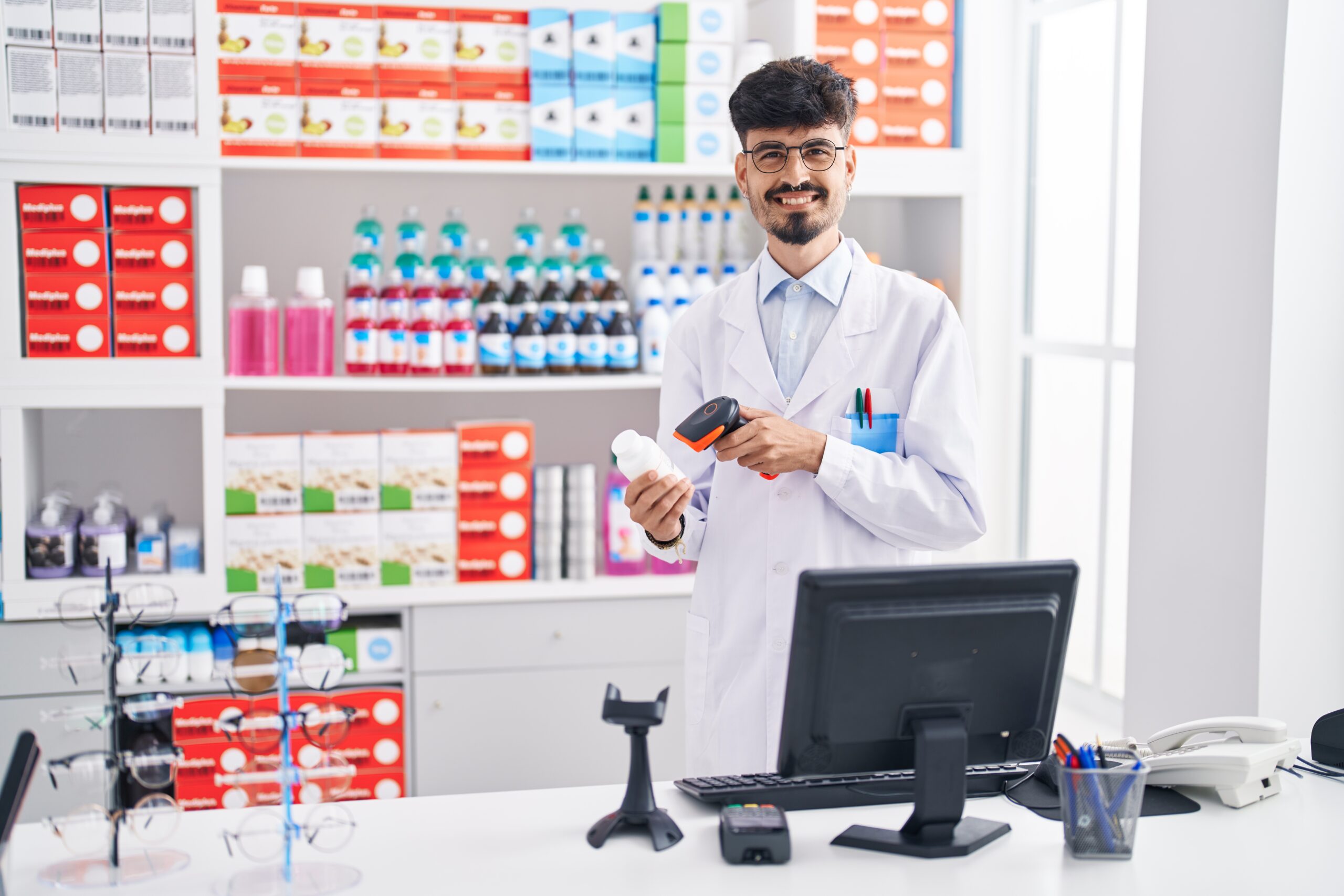 young hispanic man pharmacist smiling confident scanning pills bottle at pharmacy